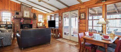 Un interior de cabaña acogedor con chimenea, televisor y comedor.