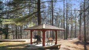 Un pabellón con una mesa y sillas, rodeado de un bosque.