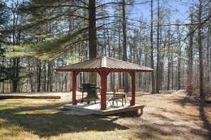 Un pabellón con una mesa y sillas, rodeado de un bosque.
