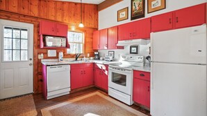Una cocina con paredes de madera, armarios rojos, electrodomésticos blancos y un ventanal que proporciona luz natural.