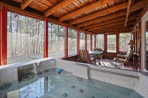 A wooden cabin with a hot tub, large windows, and a view of the forest.