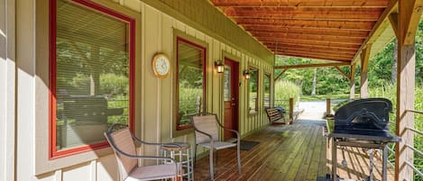 A covered porch with wooden flooring, metal chairs, a barbecue grill, and a clock on the wall.