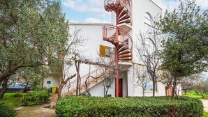 Un bâtiment doté d’un escalier en colimaçon rouge menant à un balcon, le tout entouré de verdure et d’arbres.