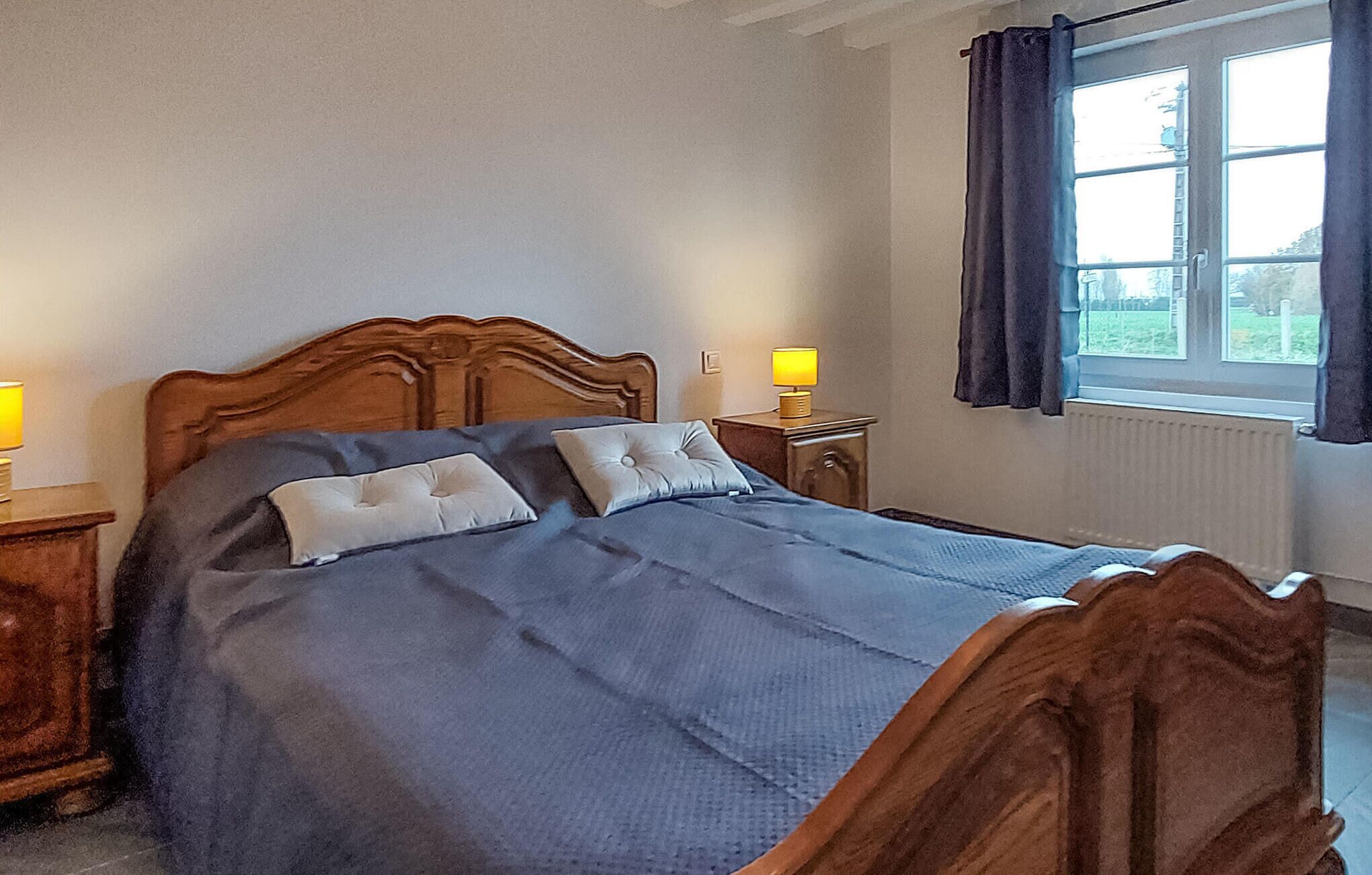A bedroom with a wooden bed, two bedside tables, a window with curtains, and a radiator.