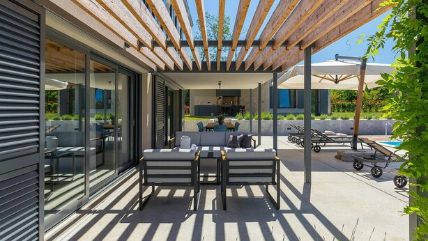 Un patio cubierto con zona de comedor, cocina al aire libre y sillones de descanso.