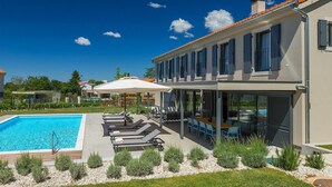 Una casa moderna de dos pisos con piscina, mobiliario exterior y un porche cubierto.
