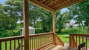 A wooden deck with a bench and a folding chair, overlooking a grassy yard with a small shed and picnic table. - Escape at Deep Hole Hideaway | Chic 2BR Retreat w/ Full Kitchen, Daybed + Sleeper Sofa, Pet Friendly (Chincoteague Island)