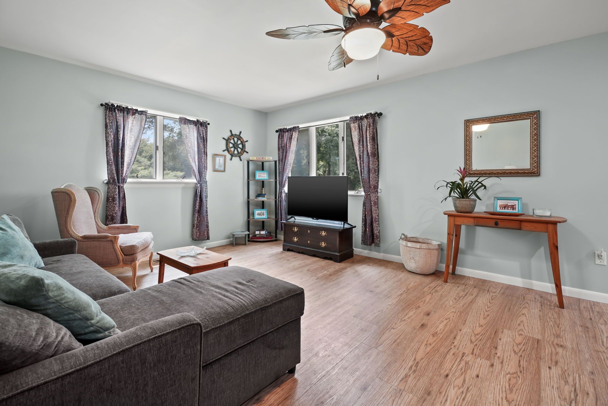 A living room with a sofa, a television, a wooden coffee table, and a ceiling fan.