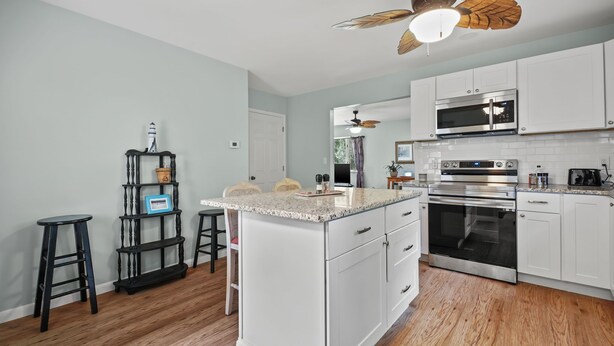 A modern kitchen with white cabinets, a central island, and a ceiling fan. - Escape at Deep Hole Hideaway | Chic 2BR Retreat w/ Full Kitchen, Daybed + Sleeper Sofa, Pet Friendly (Chincoteague Island)