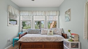 A bedroom with a wooden bed, a nightstand, a lamp, a bookshelf, and a window with blinds. - Escape at Deep Hole Hideaway | Chic 2BR Retreat w/ Full Kitchen, Daybed + Sleeper Sofa, Pet Friendly (Chincoteague Island)