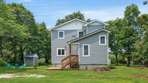 A two-story house with a front porch, a small shed, and a well-maintained lawn. - Serenity at Deep Hole Hideaway | Cozy Retreat w/ Deck, Firepit, Full Kitchen & Pet Friendly (Chincoteague Island)