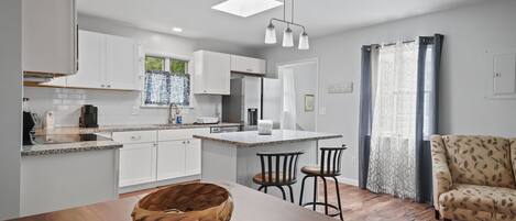 Une cuisine moderne avec des meubles blancs, un îlot central et un coin repas comprenant une table et des chaises en bois.