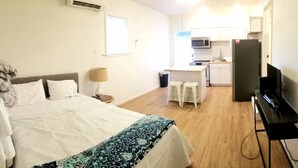 A hotel room with a bed, a desk with a computer, a TV, a kitchen area with a microwave and refrigerator, and a window providing natural light. - Magnolia #3 @ Copper Johns Resort (Lakeview)