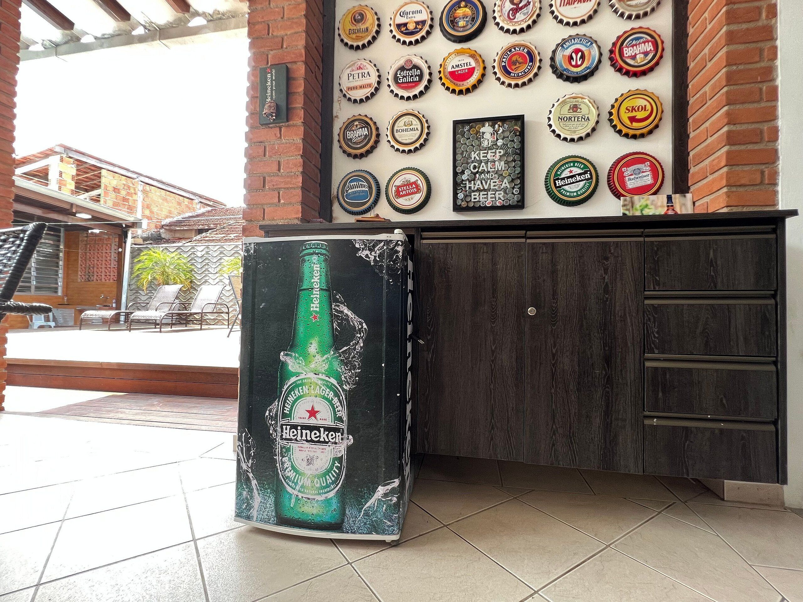A bar area with a wall of beer bottle caps and a large Heineken beer bottle decoration.