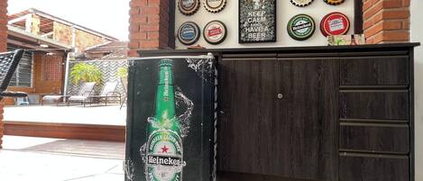 A bar area with a wall of beer bottle caps and a large Heineken beer bottle decoration.