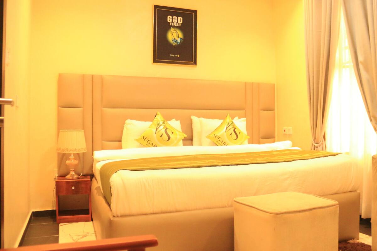 A hotel room with a large bed, a bedside table with a lamp, a chair, and a framed picture on the wall.