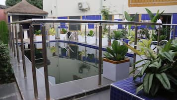 Un área de piscina con barrera de cristal, plantas en macetas y una estructura de techo de paja.