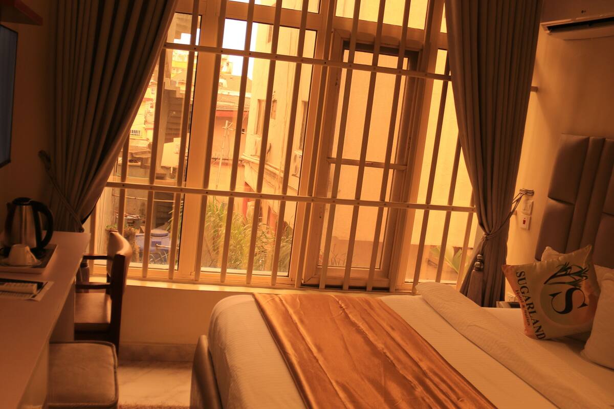 A hotel room with a bed, a desk, a chair, a TV, and a window with bars.