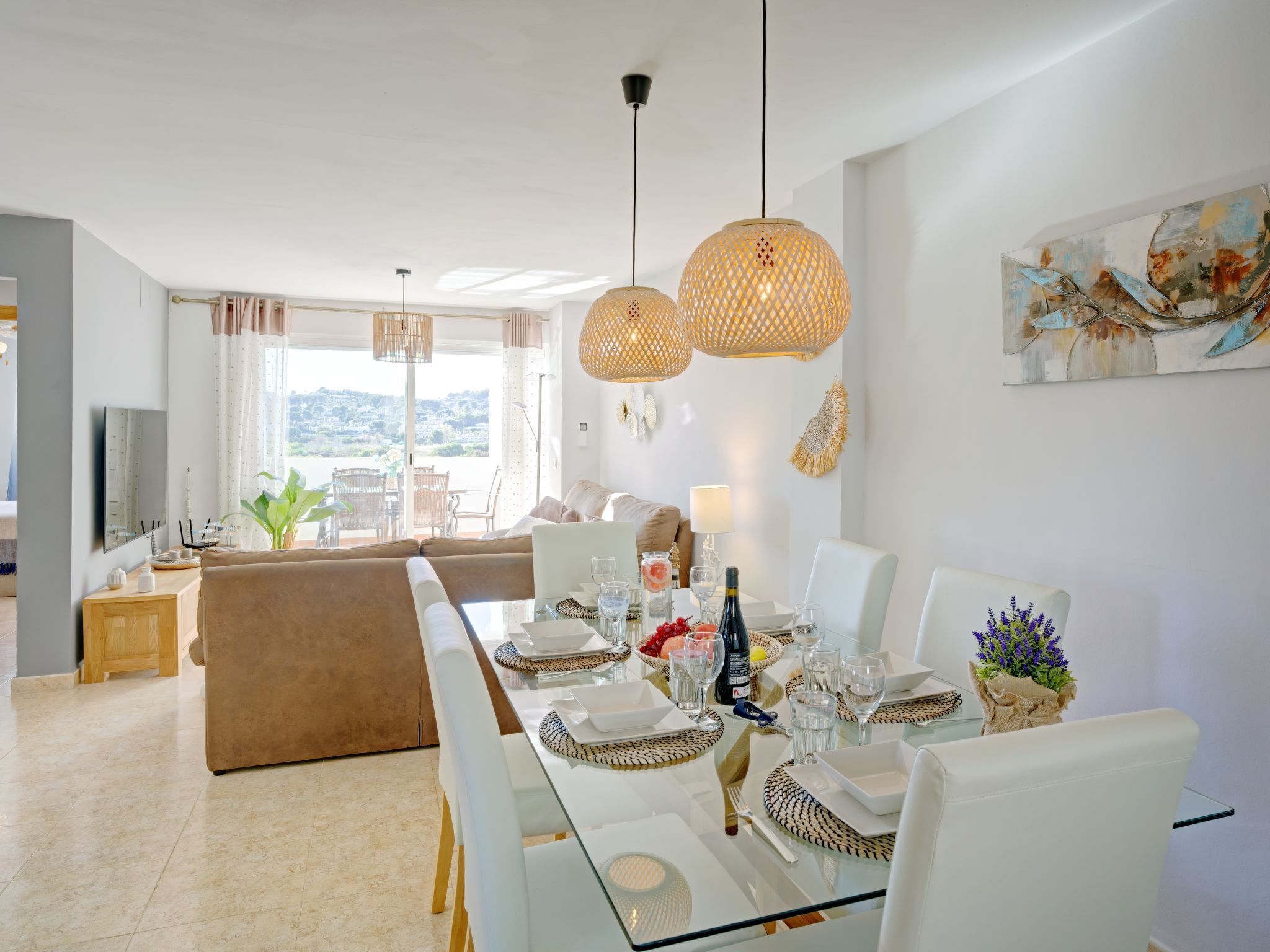 A modern dining area with a long table set for six, surrounded by white chairs.