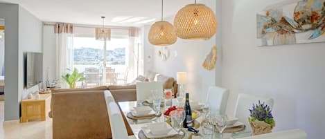 Un espace repas moderne avec une longue table dressée pour six personnes, entourée de chaises blanches.