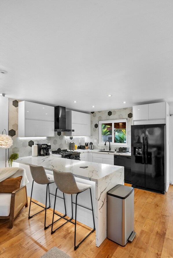 A modern kitchen with white cabinets, a black refrigerator, and a marble island with bar stools.