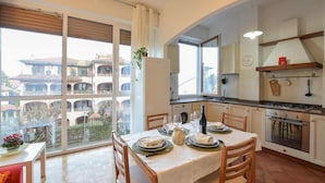 Une cuisine moderne avec un coin repas, de grandes fenêtres et une vue sur un immeuble d’habitation.