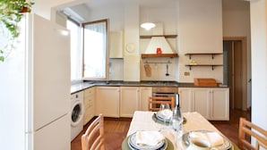 Une cuisine compacte avec un coin repas, un lave-linge et une horloge au mur.