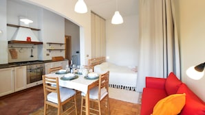 Un espace de vie compact comprenant une cuisine, un coin repas et un canapé rouge.