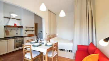 Un ambiente compatto con angolo cottura, zona pranzo e un divano rosso.