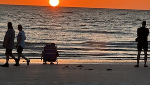 Un atardecer sobre el océano con gente caminando en la playa.