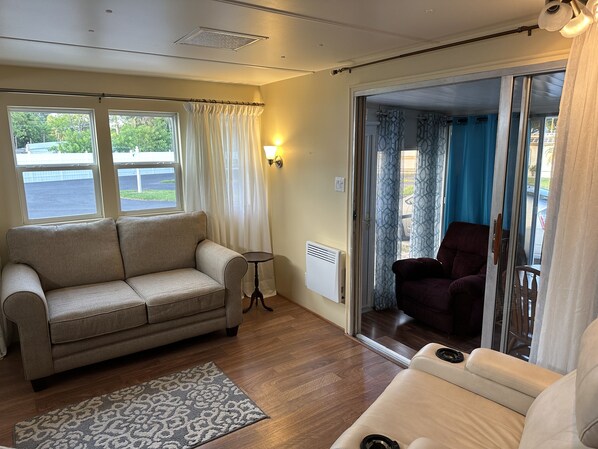 A living room with a beige sofa, a patterned rug, and a sliding glass door leading to a balcony. - Cozy little Lake Front Park Model (Port Richey)
