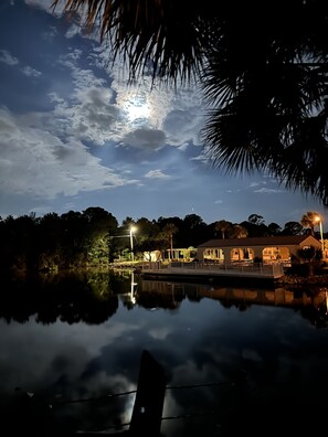A lakeside view with a building reflecting on the water, surrounded by trees and a clear sky. - Cozy little Lake Front Park Model (Port Richey)