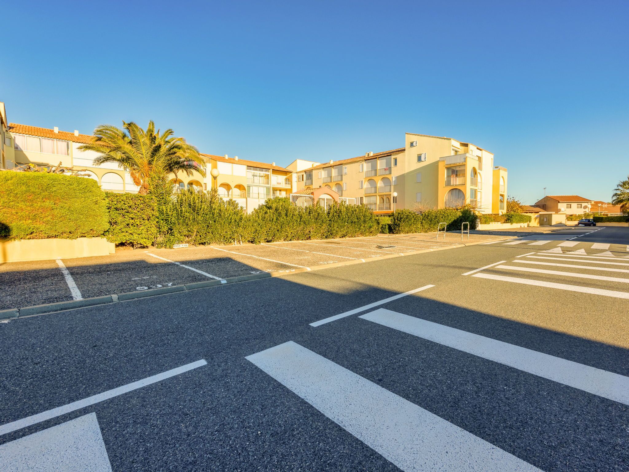 Ein Parkplatz mit Zebrastreifen und ein Gebäude im Hintergrund mit mehreren Balkonen und Fenstern.