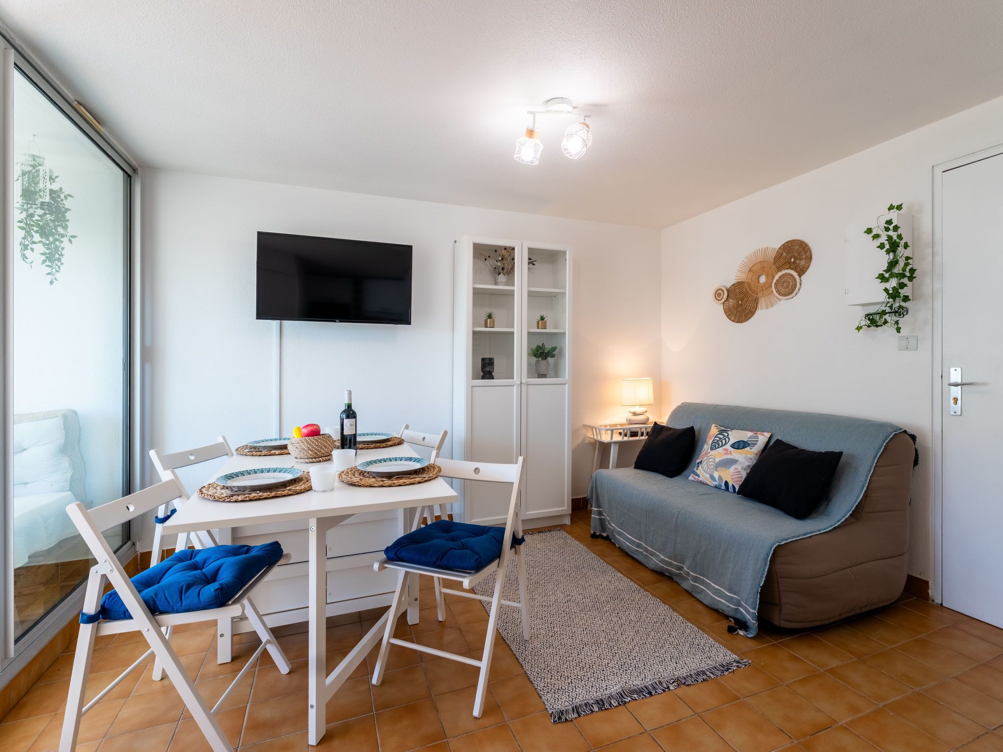 Un salon moderne avec une table à manger pour deux personnes, un canapé et un téléviseur à écran plat fixé au mur.