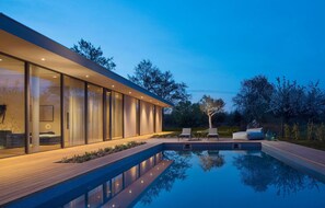 Une maison moderne dotée d’une piscine, de murs en verre et d’un espace salon extérieur.