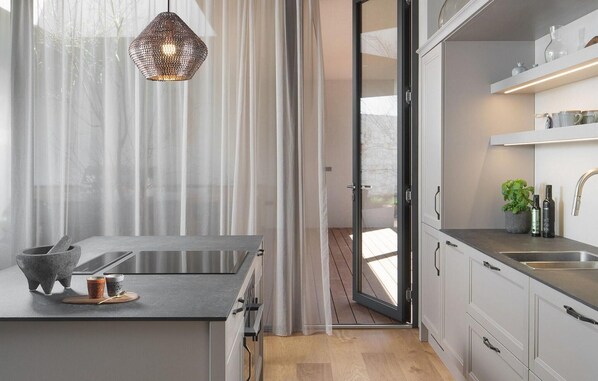Une cuisine moderne dotée d’un grand îlot central, d ’appareils électroménagers en acier inoxydable et offrant une vue à travers une porte vitrée.
