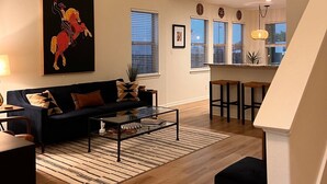 A modern living room with a dark sofa, a glass coffee table, and a chandelier.