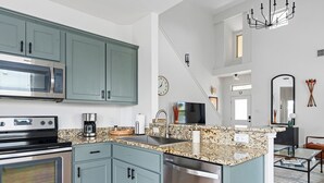 A modern kitchen with teal cabinets, stainless steel appliances, granite countertops, and a central island with a sink.