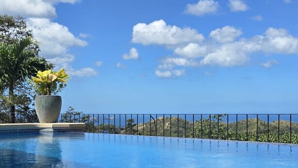 A clear blue sky with a few clouds, a swimming pool with a tiled edge, and a potted plant on the left. - Housekeeping•BBQ•Pool•4 TVs•Garden•Oceanview villa: Casa Sol Azul (Potrero)