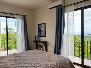 A bedroom with a large bed, a desk, and a view of the outdoors.