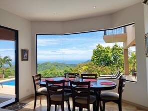 A dining area with a table and chairs, a view of a mountainous landscape, and a pool outside.