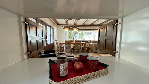 Un coin repas avec une table dressée pour deux personnes, agrémenté d'un plateau en osier contenant des bocaux et des pommes.