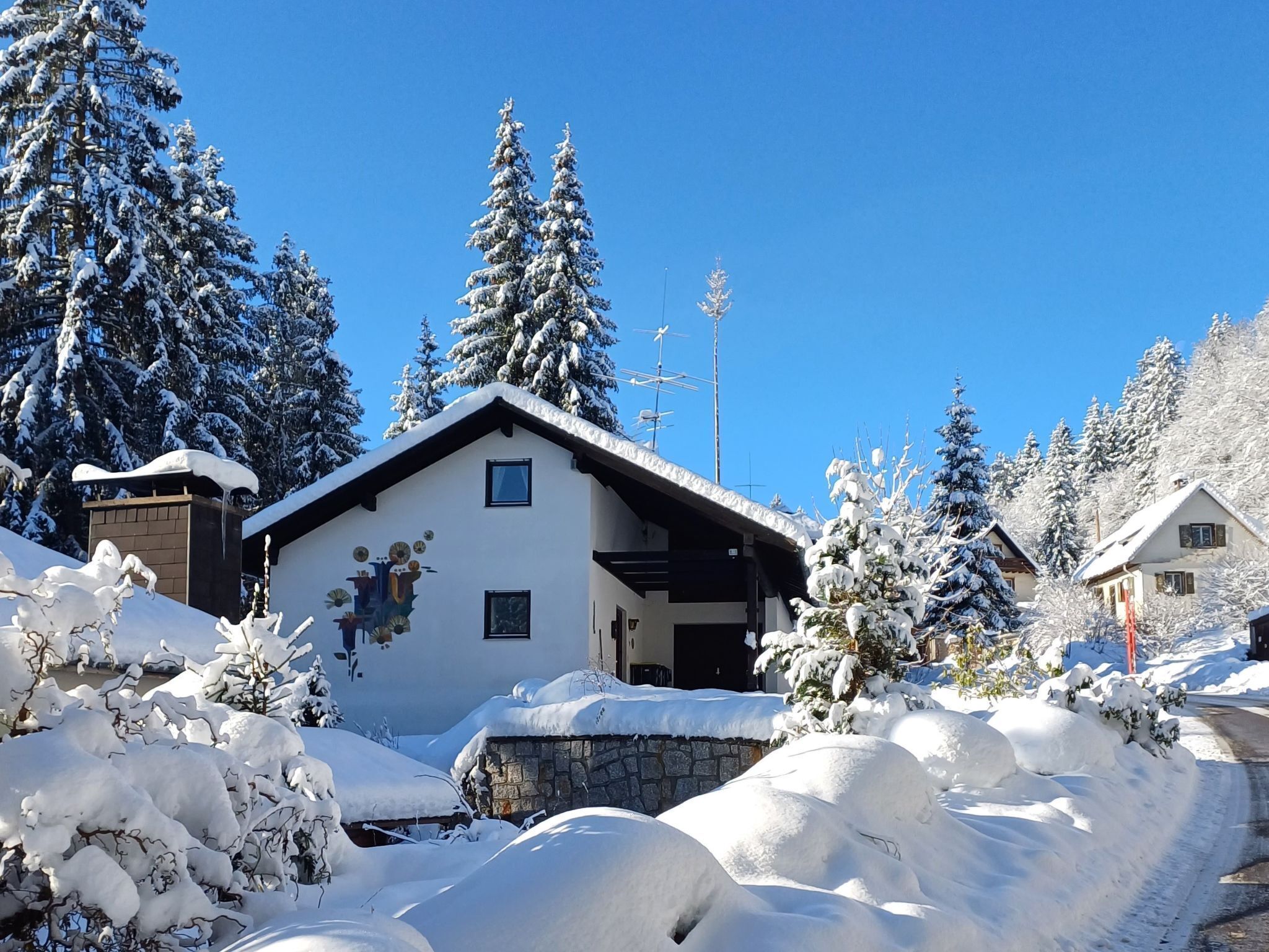 Een gebouw bedekt met sneeuw, met een stenen muur aan de voorzijde, omringd door met sneeuw beladen bomen en een helderblauwe lucht.
