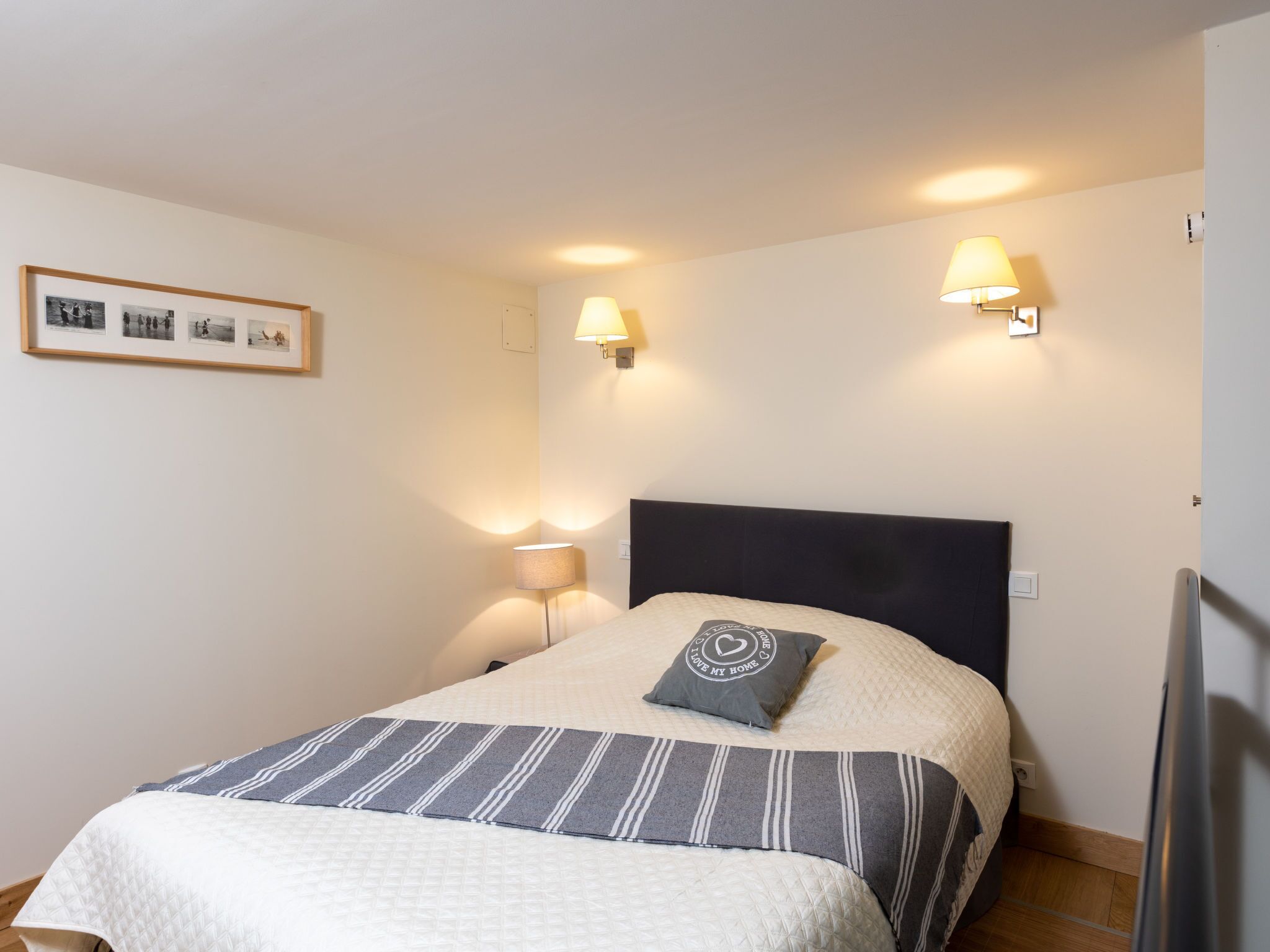 A neatly made bed with a striped blanket, two bedside lamps, and a framed photo on the wall.