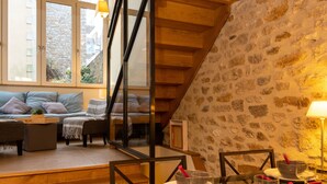 A cozy living room with a stone wall, wooden staircase, and a dining area with a glass table. - Villa Campo Bello by Interhome (Dinard)