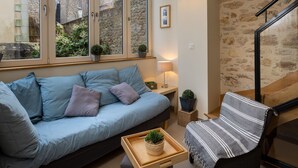 A cozy room with a blue sofa, a wooden coffee table with a plant, a lamp, and a view of a stone wall and buildings outside. - Villa Campo Bello by Interhome (Dinard)