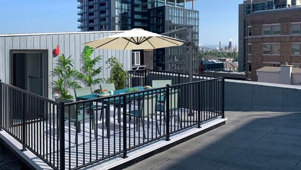 A rooftop terrace with a table and chairs, a large umbrella, and a view of surrounding buildings. - Modern Loft - Downtown Québec City (Québec)