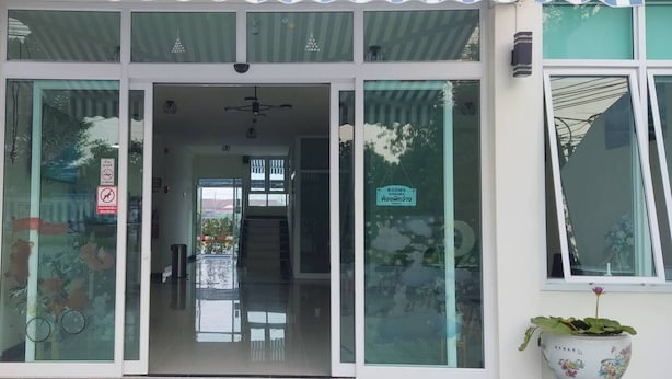 L’entrée d’un hôtel, avec des portes en verre, une pancarte indiquant que des chambres sont à vendre, et des plantes en pot de chaque côté.