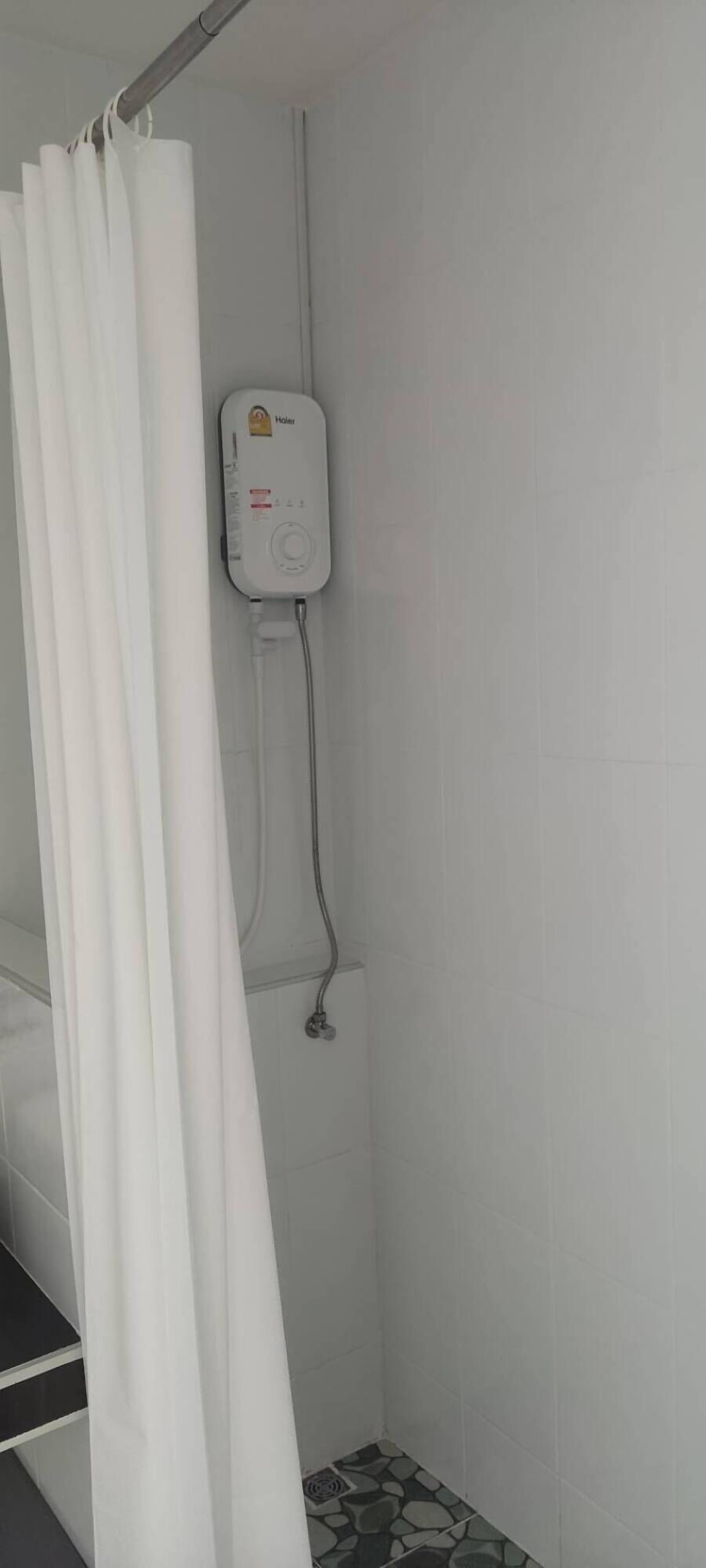 Zona de ducha con cortina blanca, cabezal de ducha de mano y panel de control en la pared.
