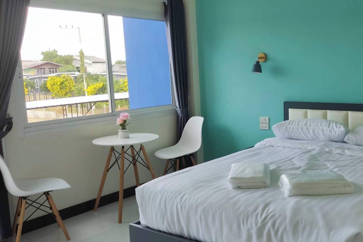 Habitación de hotel con cama, una mesita con silla, ventana con cortinas y vistas al exterior.